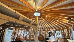 Une yourte dotée d’un plafond en bois, d’un luminaire central, d’un canapé, d’une table et d’une cheminée.