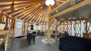 Un interior amplio y luminoso con techo alto y vigas de madera, que incluye una zona de estar central con sofás y una mesa de comedor.