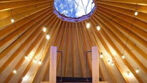 Una yurta acogedora con una escalera de madera que lleva a una cama, una pequeña mesa de madera y una ventana con vistas a árboles.