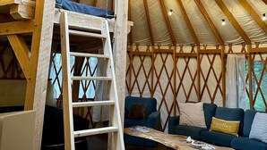 A yurt interior with a wooden ladder, a couch, and a table. - The Sunday River Glamping Yurt in Western Maine (Bethel)