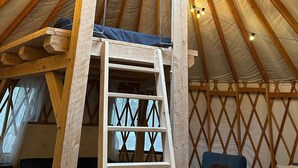 A yurt interior with a wooden ceiling, a skylight, a ladder, and a couch. - The Sunday River Glamping Yurt in Western Maine (Bethel)