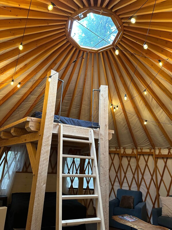 Interieur van een joert met houten plafond, dakraam, een ladder en een bank.