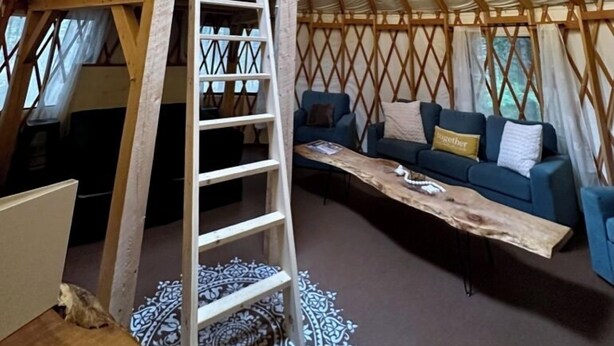 A yurt with a wooden interior, a central skylight, a ladder, a sofa, and a coffee table. - The Sunday River Glamping Yurt in Western Maine (Bethel)