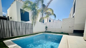 A rectangular swimming pool with clear blue water, surrounded by a tiled deck and a grassy area.