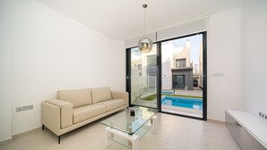 A modern living room with a glass coffee table, a beige sofa, and a large sliding glass door leading to a pool.