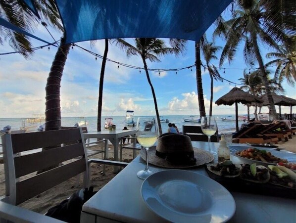 A beachside dining setup with a table, chairs, and a view of the ocean.
