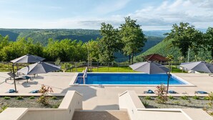 A swimming pool with a view of a mountainous landscape, surrounded by lounge chairs and umbrellas. - Luxury Villa Phoenix with Pool (Labin)