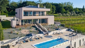 A modern two-story building with a swimming pool, outdoor seating, and a vineyard in the background. - Luxury Villa Phoenix with Pool (Labin)