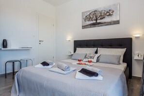 Ein ordentlich bezogenes Bett mit Kissen, ein Nachttisch mit Lampe und ein Bild an der Wand.