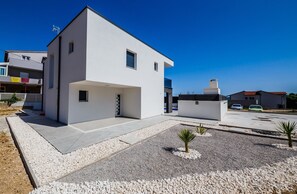 Uma casa moderna de dois andares com telhado plano, um pequeno alpendre e uma entrada para carros.