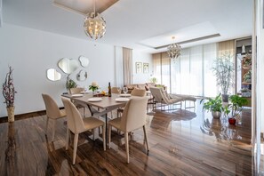 A modern dining area with a wooden table, beige chairs, and a chandelier.