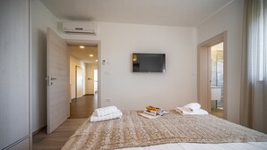Ett hotellrum med en säng, en platt-TV som är monterad på väggen och utsikt över en korridor och ett annat rum genom en öppen dörr.