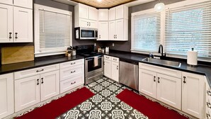 Une cuisine moderne avec des armoires blanches, un comptoir noir, un carrelage décoratif et un ventilateur de plafond.