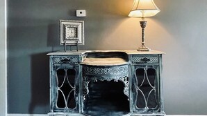 Une table d’appoint bleu foncé, richement décorée, sur laquelle est posée une lampe, et qui est placée contre un mur gris.
