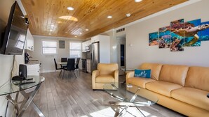 Una sala de estar moderna con techo de madera, una mesa de centro de vidrio, un sofá color beige y un televisor montado en la pared.