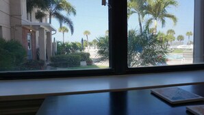 Vista a través de una ventana que muestra un edificio, palmeras y una piscina en el exterior.