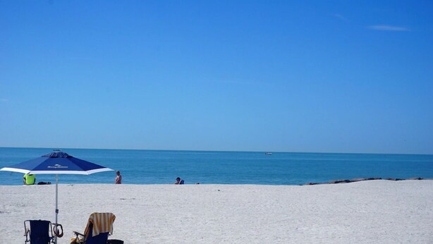 Una playa con cielo despejado, algunas personas y un paraguas azul.
