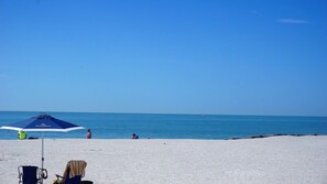 Una playa con cielo despejado, algunas personas y un paraguas azul.