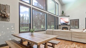 A spacious living room with a large window, a fireplace, a sofa, and a wooden table. - Island Park Cabin with Private Dock on the Lake (Island Park)