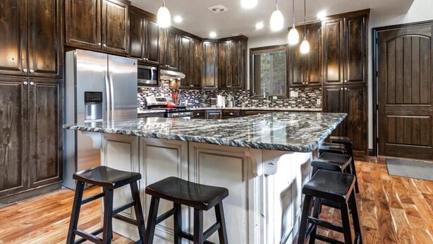 A modern kitchen with dark wood cabinets, a large island with bar stools, stainless steel appliances, and pendant lighting. - Island Park Cabin with Private Dock on the Lake (Island Park)