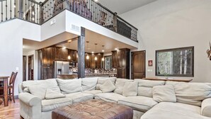 A spacious living room with a large sectional sofa, a leather ottoman, and a view of the kitchen and dining area. - Island Park Cabin with Private Dock on the Lake (Island Park)