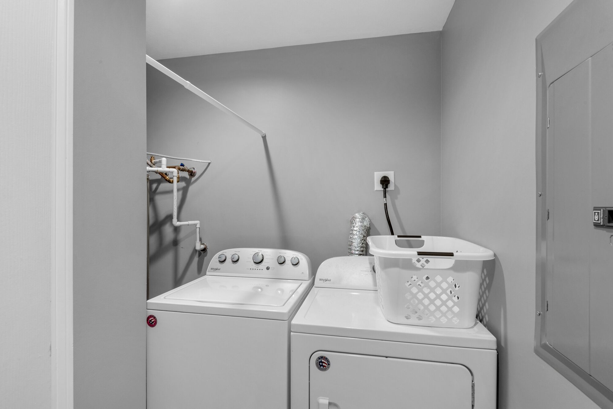 Una lavanderia con due lavatrici Whirlpool bianche, uno stendibiancheria e un cesto per la biancheria.