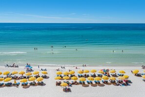 Ein Strand mit vielen gelben Sonnenschirmen und blauen Liegestühlen.
