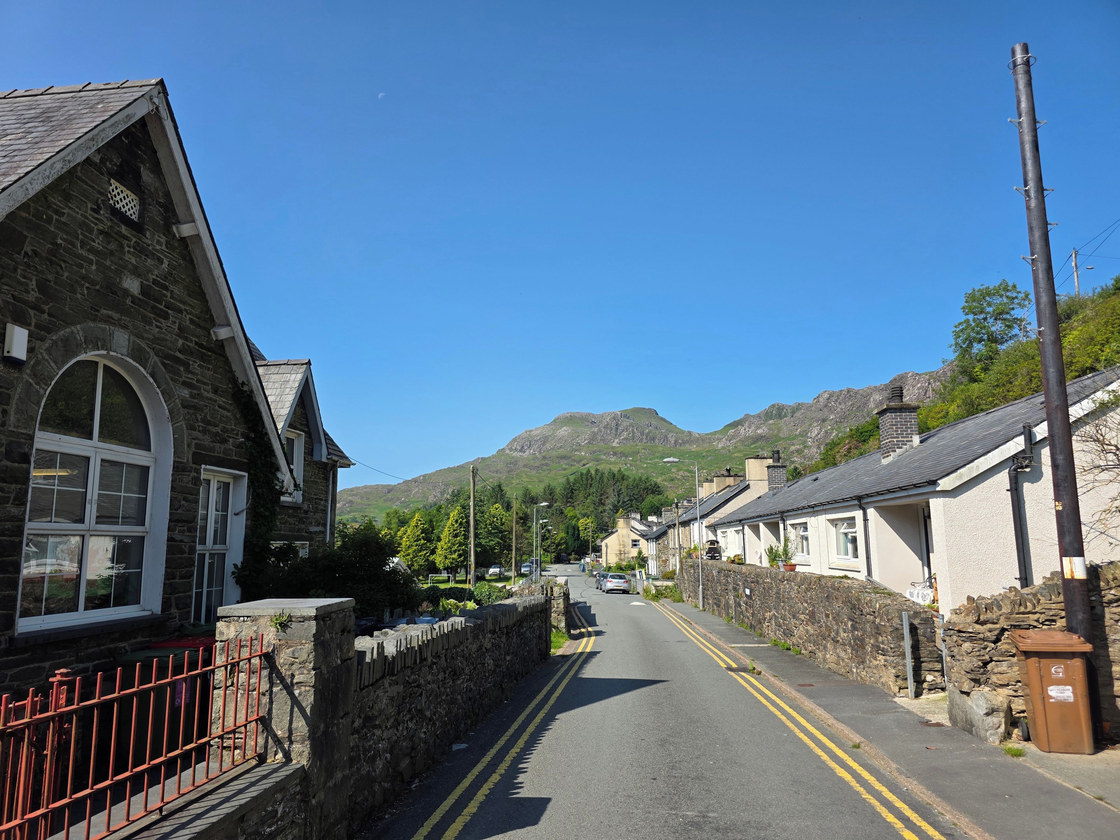 A narrow street with stone buildings, a stone wall, and a mountain in the background.