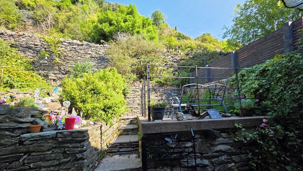 Eine Steintreppe führt zu einem Gartenbereich mit Blumentöpfen und einem Metallstuhl.