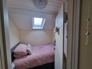 Une petite chambre à coucher accueillante, dotée d’un puits de lumière, d’un lit avec une literie rose et d’un plafond en bois.