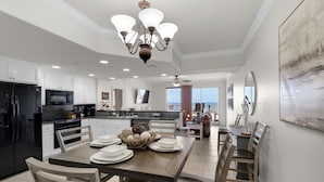 A modern kitchen with white cabinetry, a black refrigerator, and a dining area with a wooden table and chairs. - Treasure Island 0104 (Panama City Beach)