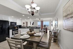 A modern kitchen with white cabinetry, a black refrigerator, and a dining area with a wooden table and chairs. - Treasure Island 0104 (Panama City Beach)