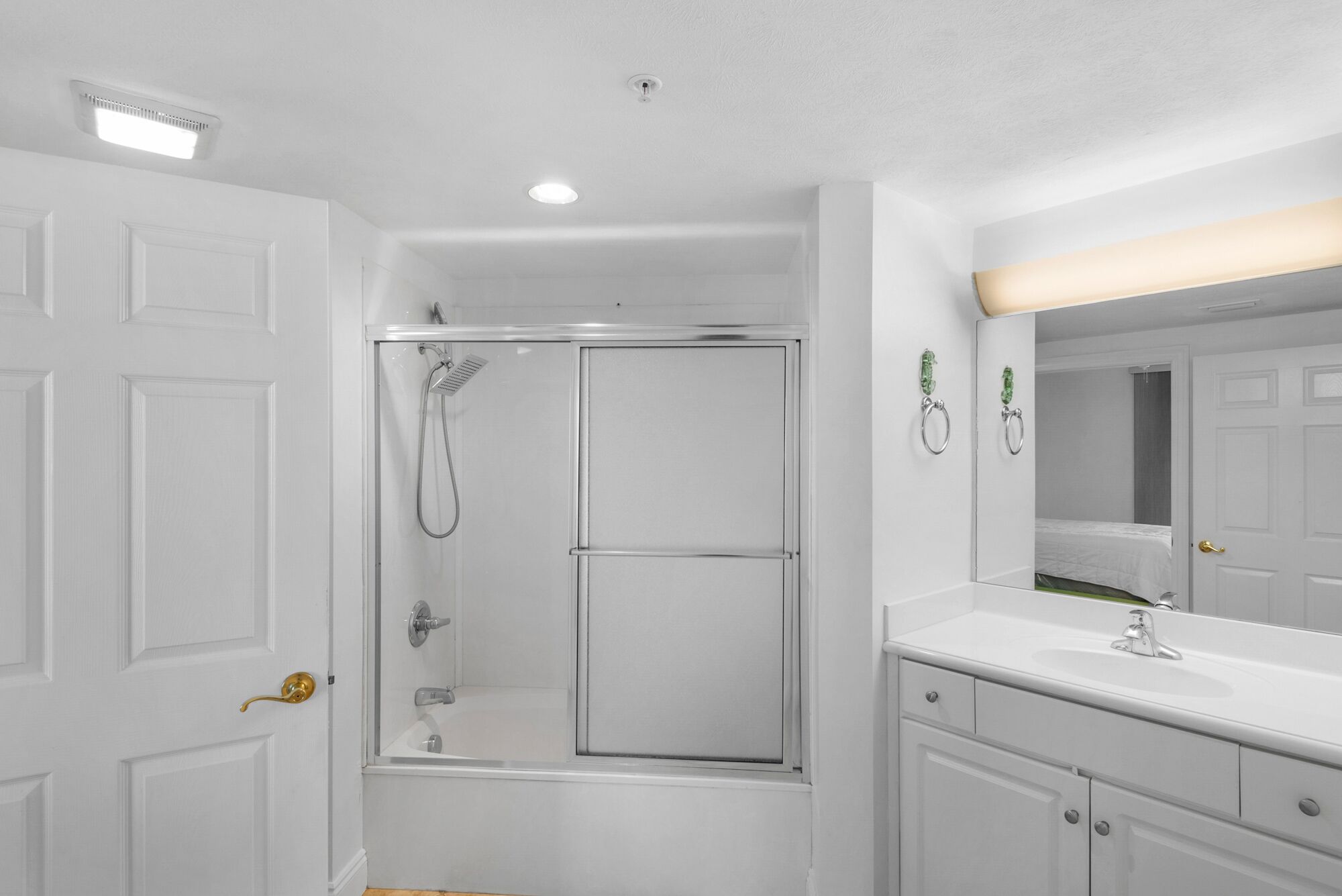 A bathroom with a walk-in shower, a sink with a mirror, and a door with a brass handle.