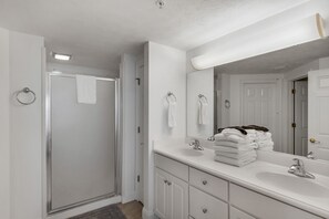 Une salle de bain moderne avec une douche à l’italienne, un grand miroir et une pile de serviettes soigneusement pliées.
