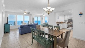 Ein geräumiges Wohnzimmer mit großem Fenster zum Meerblick, ein Essbereich mit Holztisch und Stühlen sowie eine Küche mit weißen Schränken und Edelstahlgeräten.