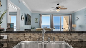 A modern kitchen with a double sink, a ceiling fan, and a view of the ocean. - Treasure Island 1904 (Panama City Beach)