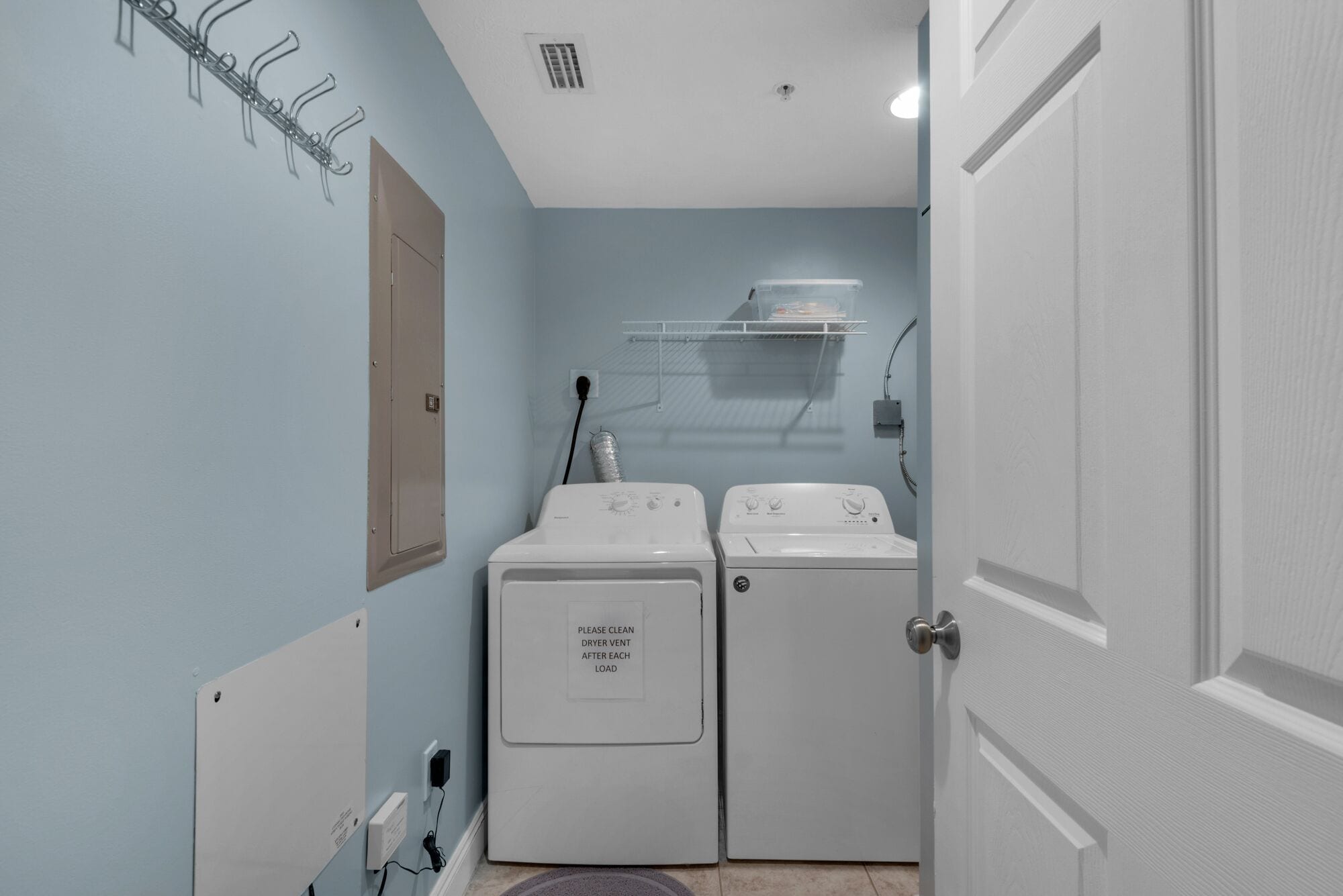 A laundry room with two white dryers, a metal rack, and a door.