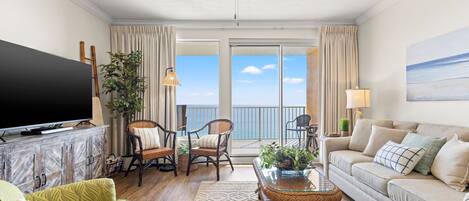 Una sala de estar con televisor, dos sofás, una mesa de centro y un balcón con vistas al mar.
