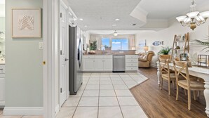 Une cuisine moderne avec des meubles blancs, un réfrigérateur en acier inoxydable et un coin repas comprenant des chaises en bois et un lustre.