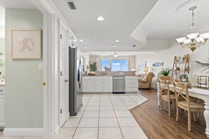 A modern kitchen with white cabinets, a stainless steel refrigerator, and a dining area with wooden chairs and a chandelier.