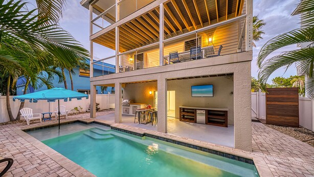 A two-story house with a swimming pool, outdoor seating, and a TV mounted on the wall. - 🌴 Island Escape | Home on Siesta Key w/ Private Heated Pool & Ping Pong Table! (Siesta Key)