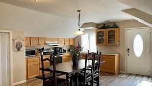 A spacious kitchen with wooden cabinets, a dining table with chairs, and a hanging light fixture. - Spacious & Modern with Workspace - A+ Location!!! (Mooresville)