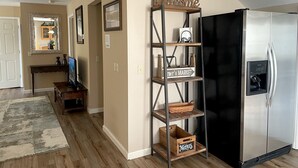 A kitchen with a stainless steel refrigerator, a wooden shelf with 'Welcome' and 'Merius' signs, and a wooden console table with a television. - Spacious & Modern with Workspace - A+ Location!!! (Mooresville)