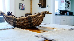 A woven basket on a wooden table with a white rug, a kitchen in the background, and a sign that reads "The Trail Properties". - The SISU Shack - 4BR Trailside Stay (Ironwood)