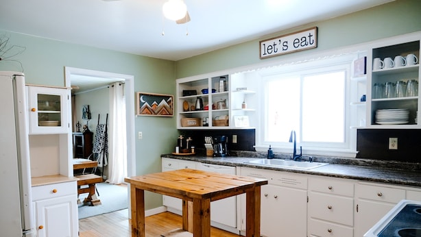 A kitchen with white cabinets, a wooden table, and a window with a 'let's eat' sign. - The SISU Shack - 4BR Trailside Stay (Ironwood)