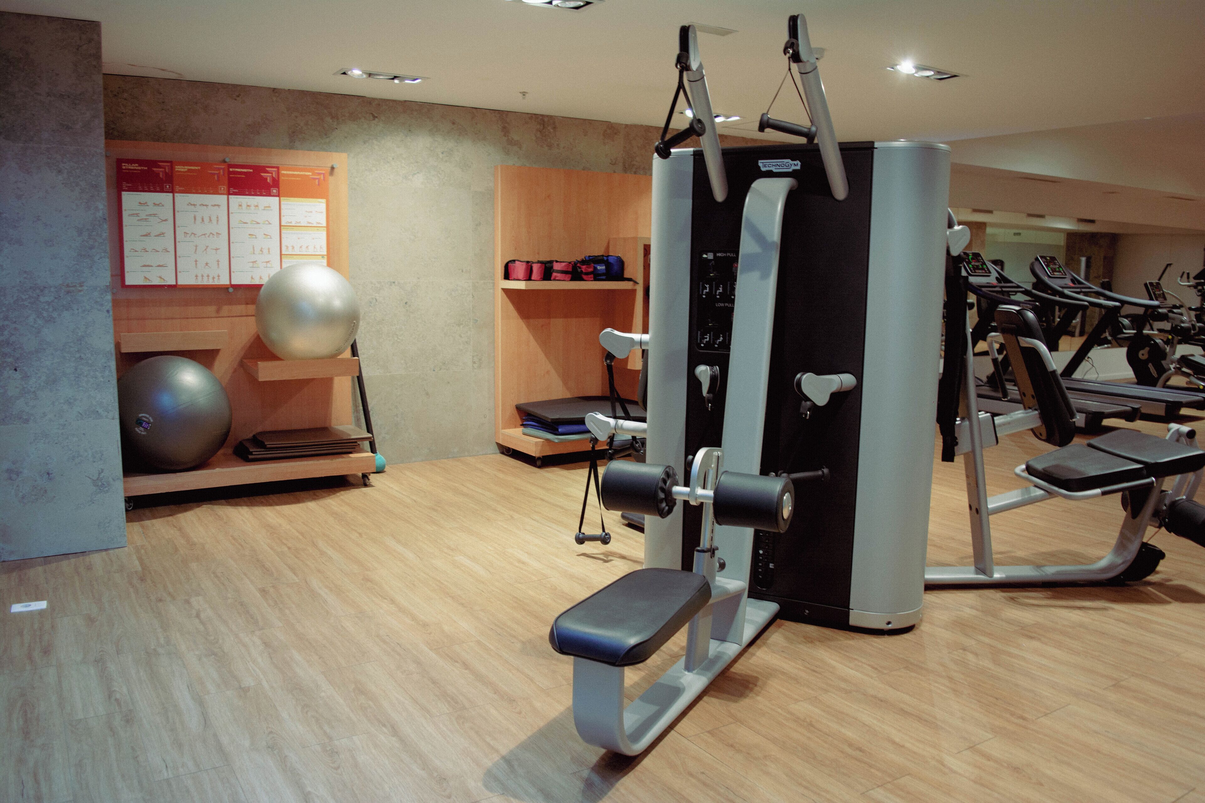 Une salle de sport équipée de matériel d’exercice, un tableau affichant les horaires et une étagère en bois où sont posés des sacs.