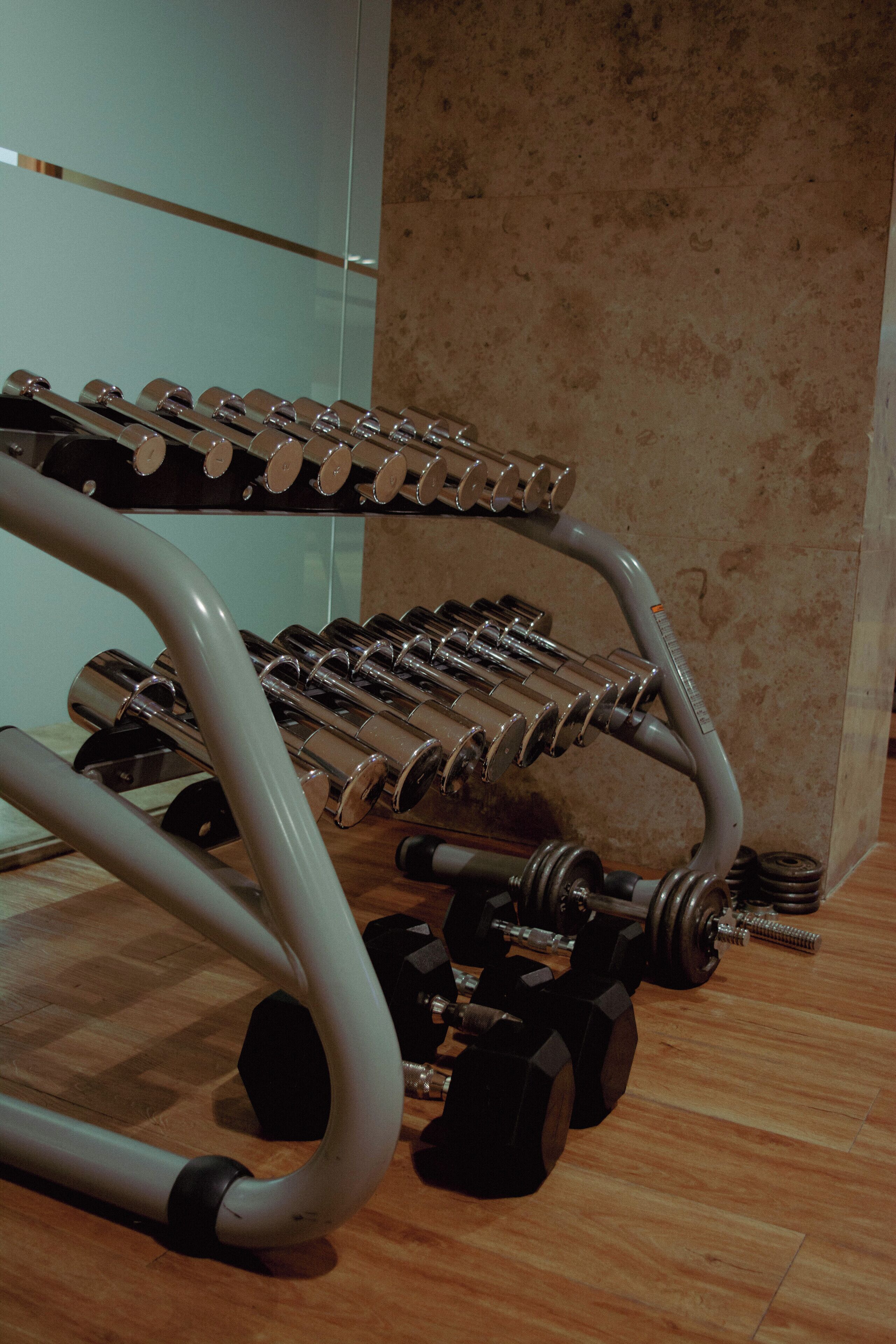 Academia com diversos equipamentos de ginástica, incluindo halteres e uma estante de pesos.