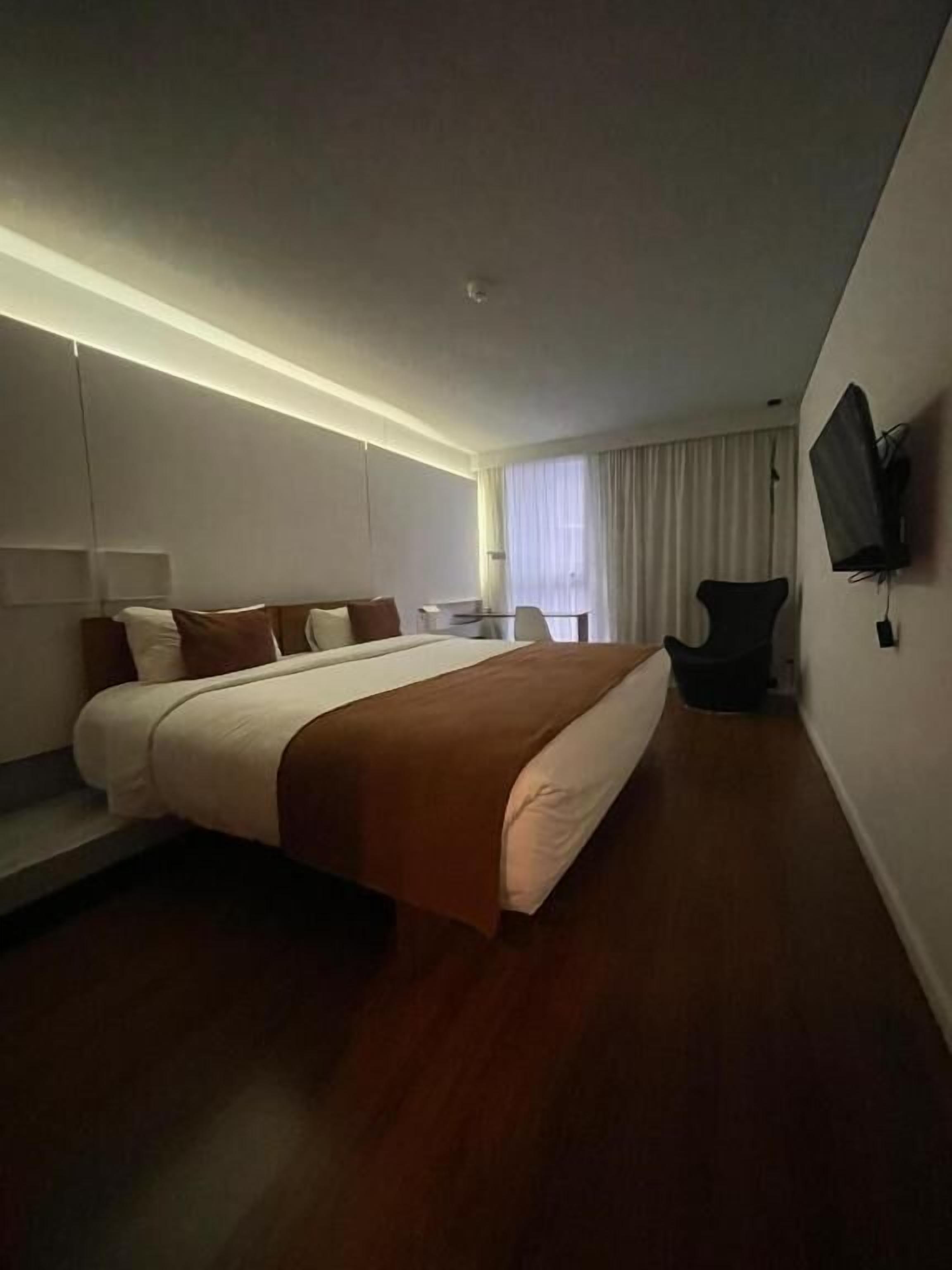 A modern hotel room with a large bed, a desk, and a TV mounted on the wall.