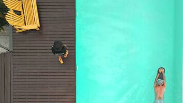 Una piscina con muelle de madera y sillones de descanso.