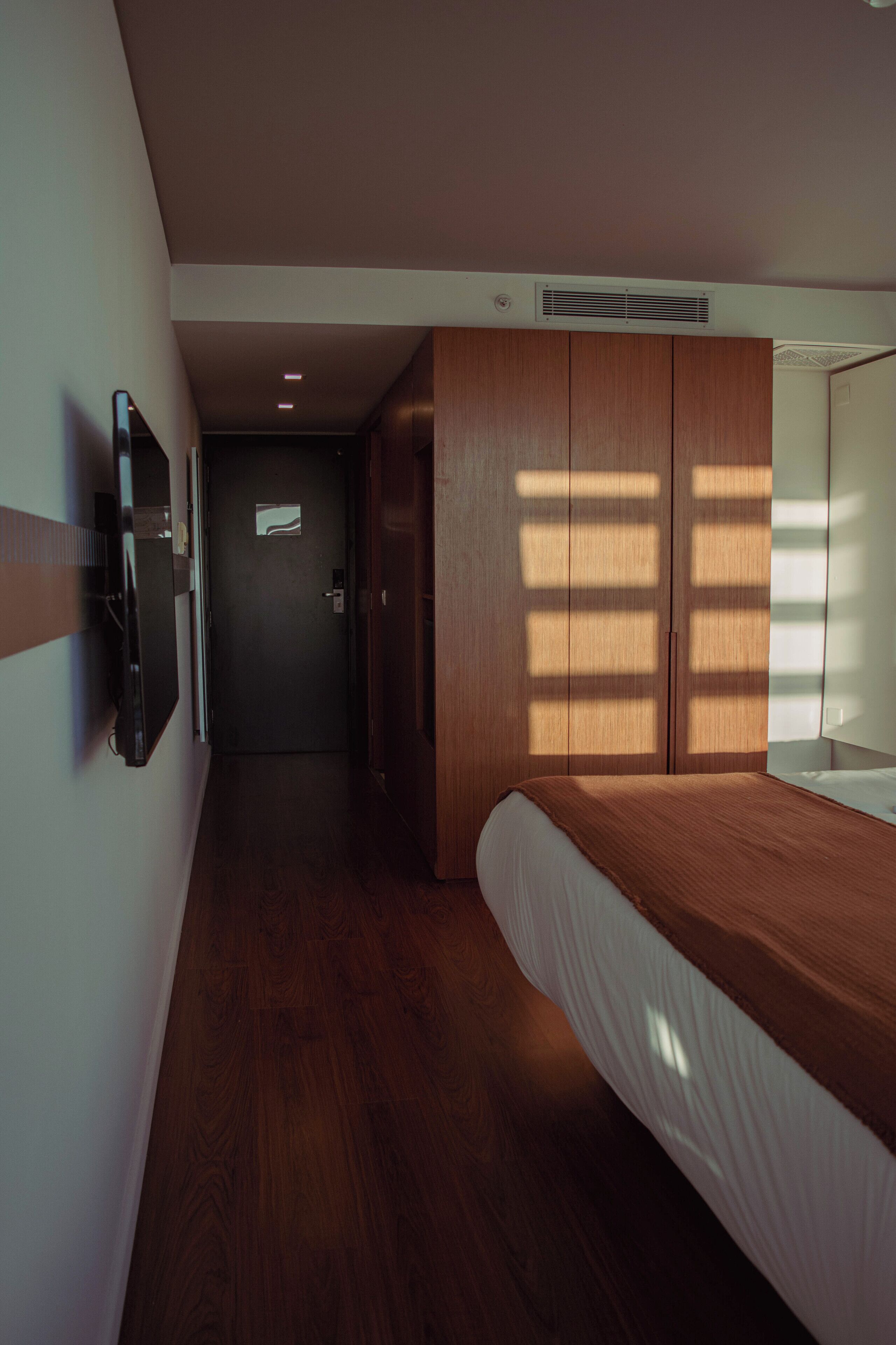 A bedroom with a bed, wooden wardrobe, and a television on the wall.